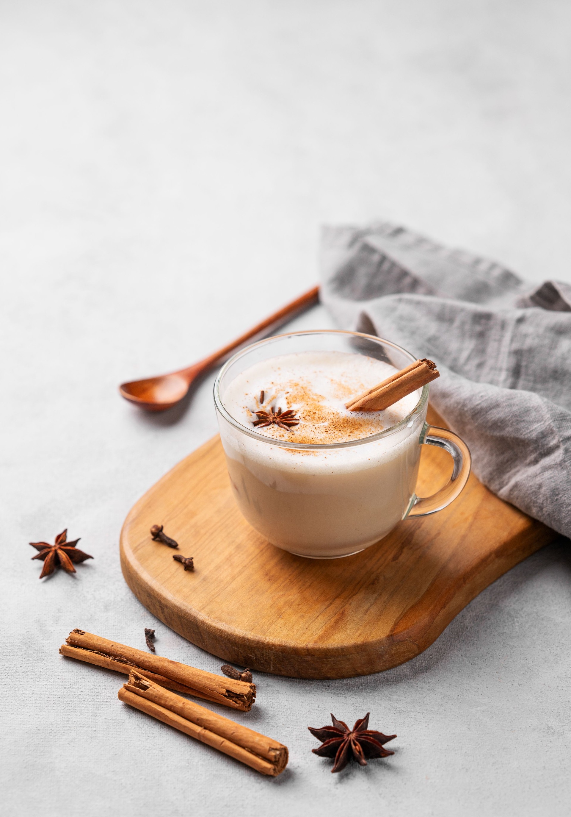 Traditional Indian masala chai latte in a glass cup. Hot drink with milk, spices and herbs on a wooden board on a light background.