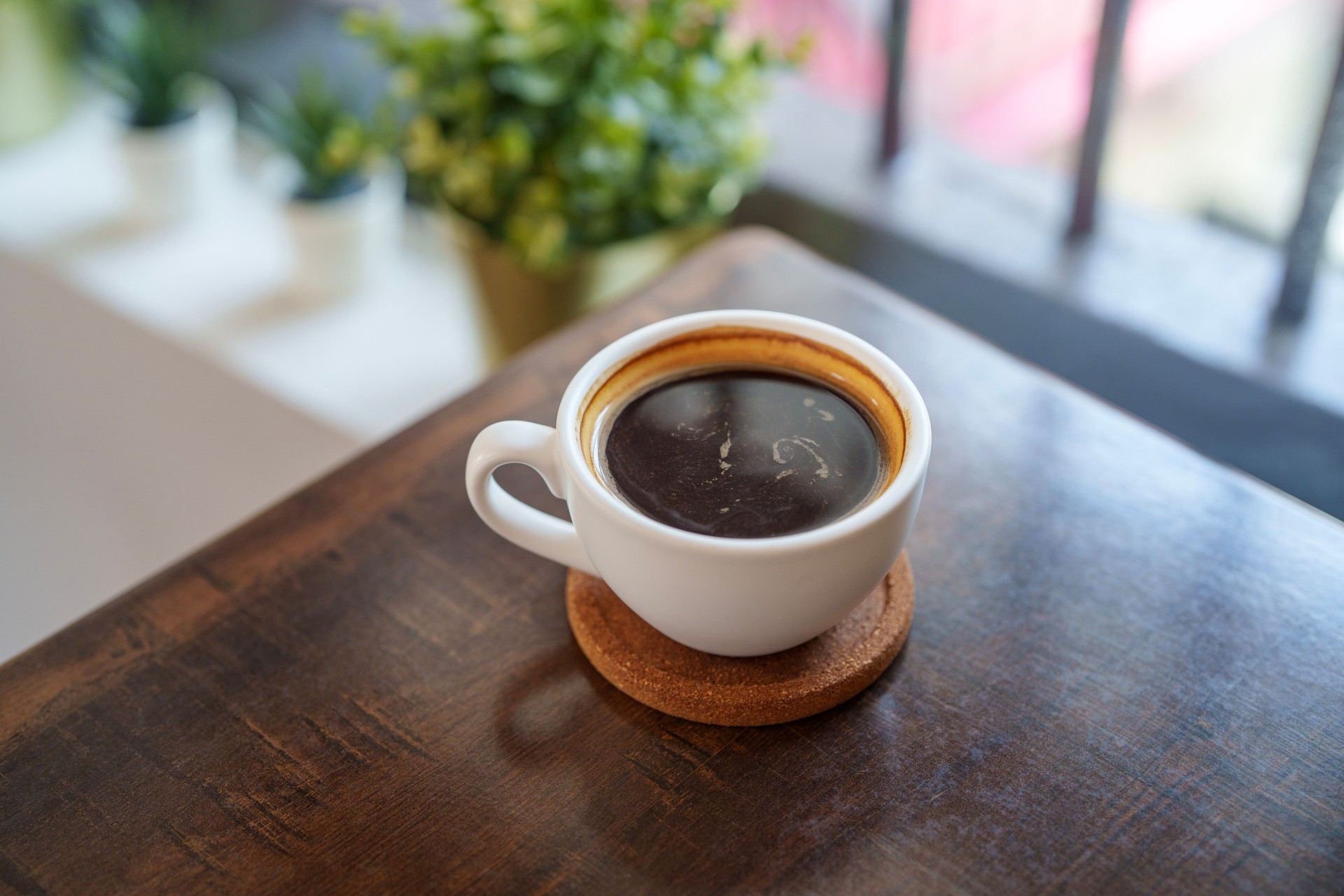 High-angle view of a cup of black coffee on a wooden table beside a window.